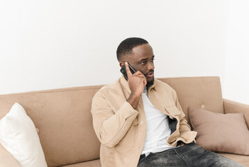 Serious black freelancer talking on the phone while working from home. Young african american businessman talking to customers on mobile phone