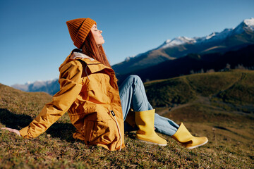 Woman sitting on a hill on the grass rest smile with teeth looking at the mountains in the snow in...
