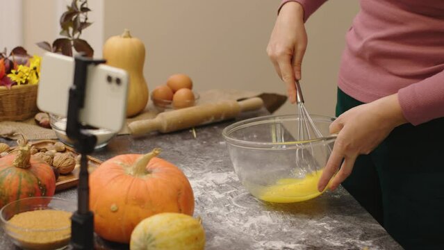 Female Blogger Shoot Video Cooking Pumpkin Pie For Thanksgiving Family Meal Phone Camera. Unrecognizable Hands Whip Eggs Beat In Bowl Using Metal Whisk. Record Video For Food Vlog Social Media Content