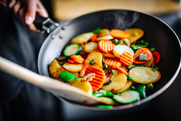 Woman cooking tasty vegetable mix stew in pan on kitchen