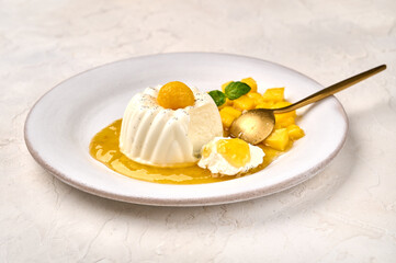 Spoon and piece of homemade panna cotta with natural vanilla pod, mango syrup and mint, selective focus