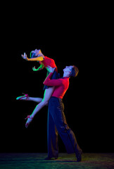 Full-length portrait of young beautiful man and woman dancing ballroom dance isolated over dark background in neon light. Concept of art, beauty, grace, action, emotions.