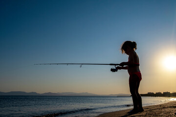 little girl is fishing with a fishing rod in the sea, under the sun. Silhouette.