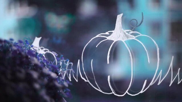 Pumpkin drawing with a white sharpie on a window glass with purple flowers and background