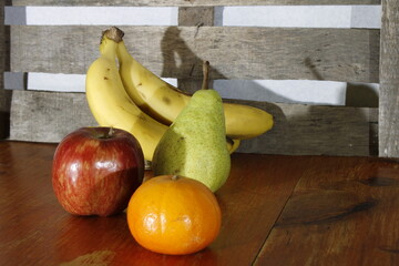 Frutas de temporada de plátanos, peras, manzanas y mandarinas en las rústicas tablas de madera con sombras suaves, forman un original diseño culinario de bodegones con un fondo rústico de madera - obrazy, fototapety, plakaty