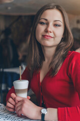 Cute brunette girl in a red blouse is sitting at a table in a cafe