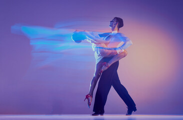 Art in motion. Flexible adorable ballroom dancers in stage attires dancing isolated on purple background in neon mixed light. Music, dance, emotions