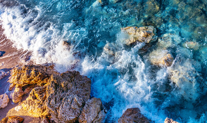 Very beautiful image of the natural beauty of the sea element - transparent waves of a turquoise hue with caps of white foam break on the coastal stones.
