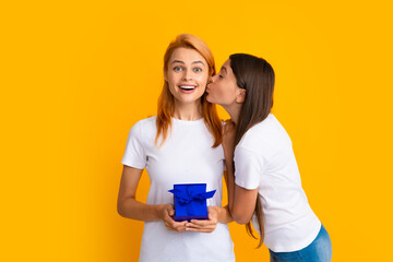 Child kissing mom. Mother and daughter with present gift. Teenager girl giving gift box to her mother on yellow background.