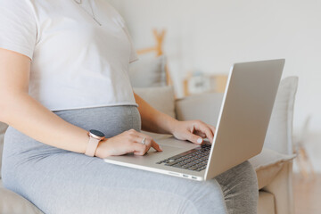 Closeup hand of pregnancy woman using online laptop on sofa with sunlight