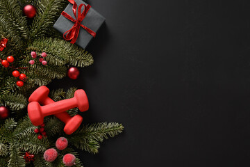 Christmas sport composition with gift and two red sports dumbbells on black background. Top view...