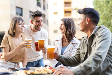 Multiracial friends drinking beer at brewery pub garden - Genuine friendship life style concept with guys and girls enjoying happy hour food together at open air bar dehor - Warm vivid filter