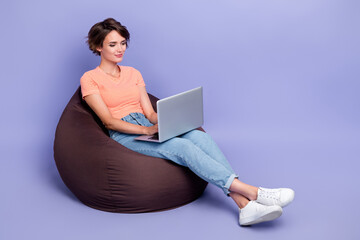 Naklejka premium Full body photo of pretty young girl work remotely laptop brown beanbag dressed stylish striped clothes isolated on purple color background