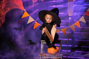 Happy Halloween. Cute cheerful little witch with a magic wand and a book of spells conjures.