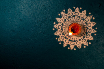Happy Diwali Festival of Lights teal color background with red and golden color traditional clay oil lamp Diya lit on white powder color Rangoli design during Deepavali celebration, wallpaper, banner. © Sunanda Malam