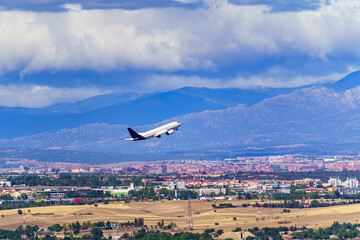 Generic Avio taking off and taking height next to a city and large mountains in the background.