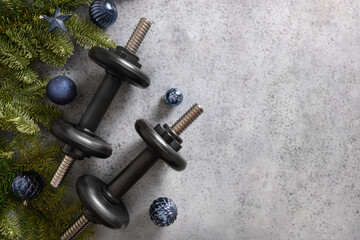 Christmas greeting card with two blue sports dumbbells, fir tree branches and gift on gray...