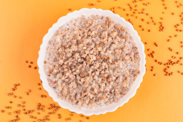 Buckwheat porridge with milk in a white bowl (plate) on an orange background. Porridge for a child (baby). Healthy breakfast.