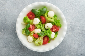 Caprese salad. Italian caprese salad with sliced tomatoes, mozzarella cheese, basil, olive oil in white plate over white background. Delicious Italian food. Top view. Rustic style.