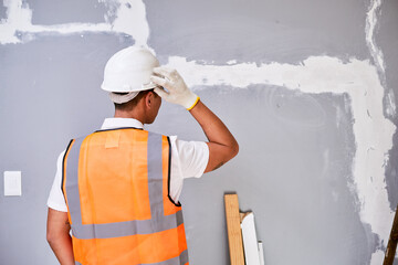 A construction worker scratches head in confusion while looking at fixed crack