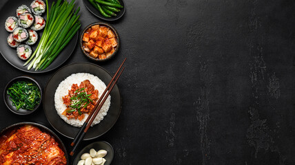 Korean food on a black background. Rice, kimchi, kimbap, pickled radish, vegetables and herbs, flat lay, banner, copy space
