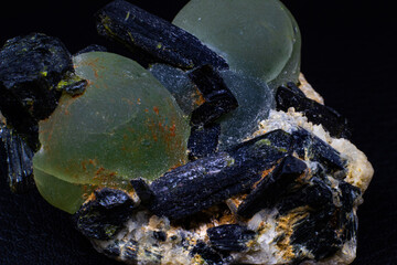 Chunk of real green prehnite spheres and dark green almost black epidote spikes on matrix macro isolated on black surface 