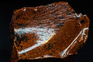 Real shiny specimen of orange Mahogany Obsidian volcanic stone macro isolated on black leather...
