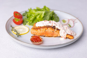 Salmon (trout) with creamy Champagne sauce with red caviar, arugula, cherry tomatoes, radish and lemon. Traditional French dish. Selective focus, close-up.