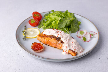 Salmon (trout) with creamy Champagne sauce with red caviar, arugula, cherry tomatoes, radish and lemon. Traditional French dish. Selective focus, close-up.