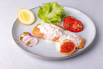 Salmon (trout) with creamy Champagne sauce with red caviar, salad, tomatoes, radish and lemon. Traditional French dish. Selective focus, close-up.