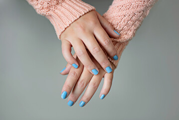 Women's hands in a coral sweater and blue manicure.