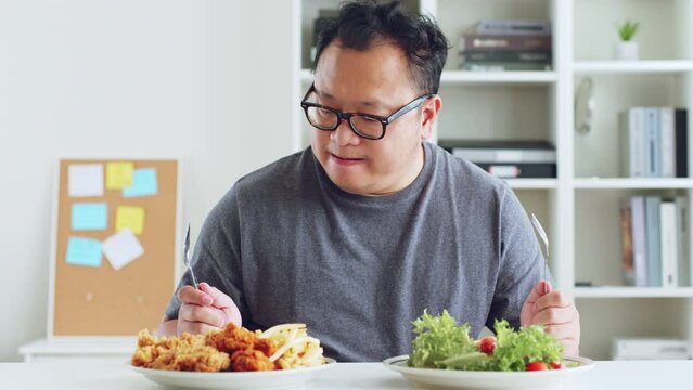 Fat asian man hesitate to eat between healthy food and junk food