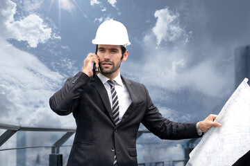 Maintenance engineer manager holds blueprint standing on rooftop construction site city skyline cloudscape background. Architect man wear safety helmet check building structure for repair project plan