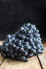 A bunch of black grapes on a wooden table on a black background, side view, close-up.