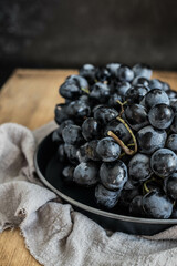 Black grapes on a tray and napkin, on a wooden table, side view. Close-up. Selective focus.