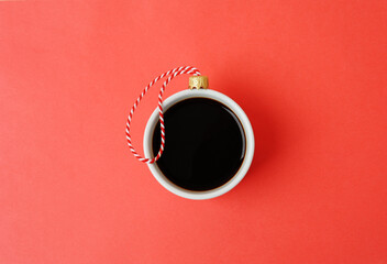 White cup of black espresso coffee decorated as Christmas ball. Close up, red background. New Year...