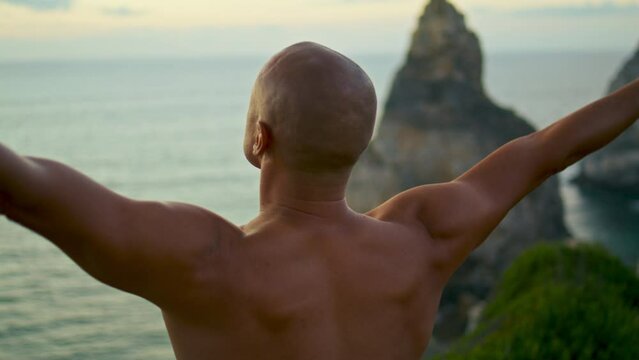 Calm yogi meditating ocean cliff closeup. Muscular athletic back at sunset sea