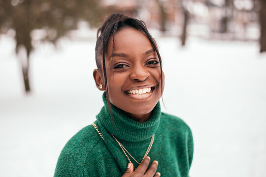 Shocked surprised amazed african american woman standing street outside with white snow background, smiling teeth. New Year atmosphere, winter vacation, cold weather
