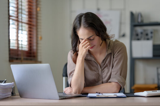 Asian Business Woman Feeling Stress At Work When Faced With Difficult And Hard Work Feeling Headaches And Eye Strain And Working On A Laptop Computer In The Office.