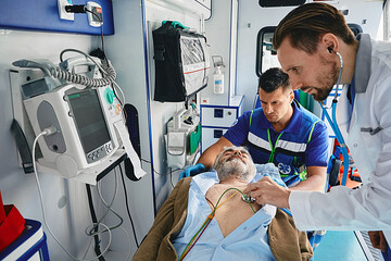 Doctor listening to heartbeat of injured patient connected to ECG monitoring equipment using stethoscope while inside ambulance with paramedic