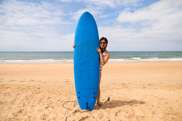 Beautiful young latin woman with blue surfboard. The woman is on the beach. Holiday and summer concept.