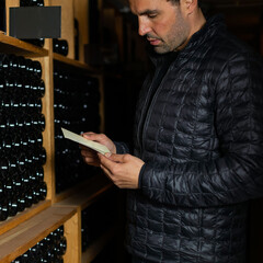 Man in the wine cellar with bottles in background drinking and tasting wine.