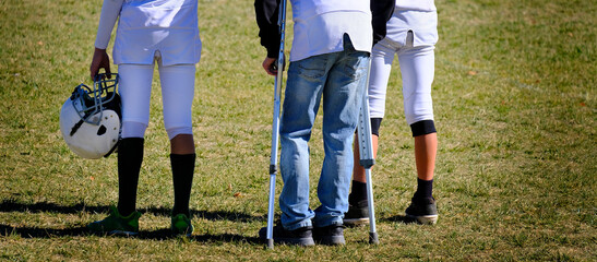 Injured Football Player on Sidelines with Crutches with Team