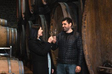 Medium view of the Caucasian couple during a wine tasting in a wine cellar, with large oak barrels...