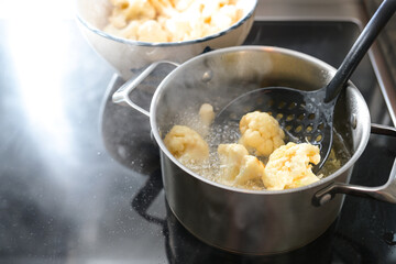 Cauliflower florets are deep fried in a pot with hot cooking oil on the stove, preparation of a...