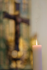 A holy candle burning in the interior of a catholic church with Jesus and the cross in the blurred background. 
Color illustration photo of Christian religion or faith.