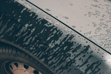 Close-up picture of stains on dark grey tin of a wet car bonnet and wheel detail. Color abstract photo of water drops surface.
