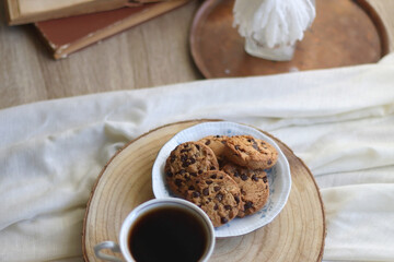 Cup of tea or coffee, plate of chocolate chip cookies, open book, reading glasses, candle and vase with flowers. Selective focus.