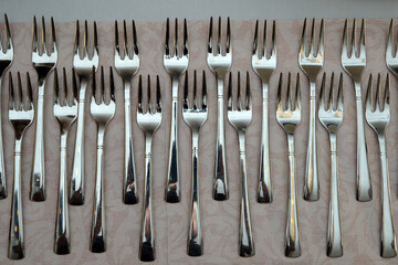 A large pile of shiny stainless steel forks neatly arranged on the laid table. Abstract illustration photo of cutlery, restaurant or catering.