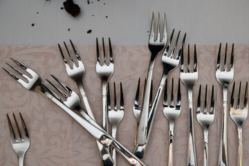 A set of stainless steel forks on the table covered with a pink cloth, with leftover cake crumbs...